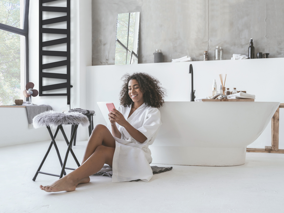 Smiling woman sitting in the bathroom on the floor with a smartphone in her hands